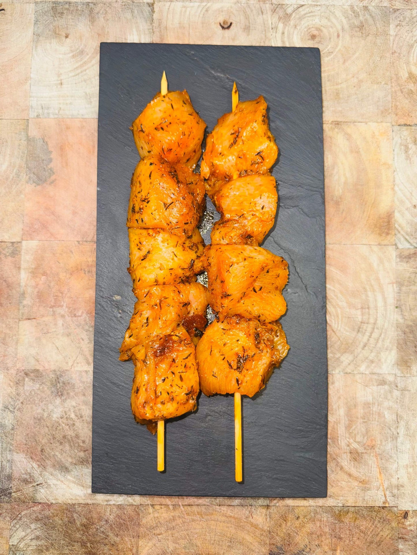 Brochettes de poulet marinées, présentées sur une planche noire, 200g, saveurs variées.