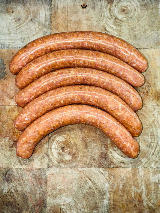 Chipolatas Piment d'Espelette, origine France, 500g sur planche de bois rustique.